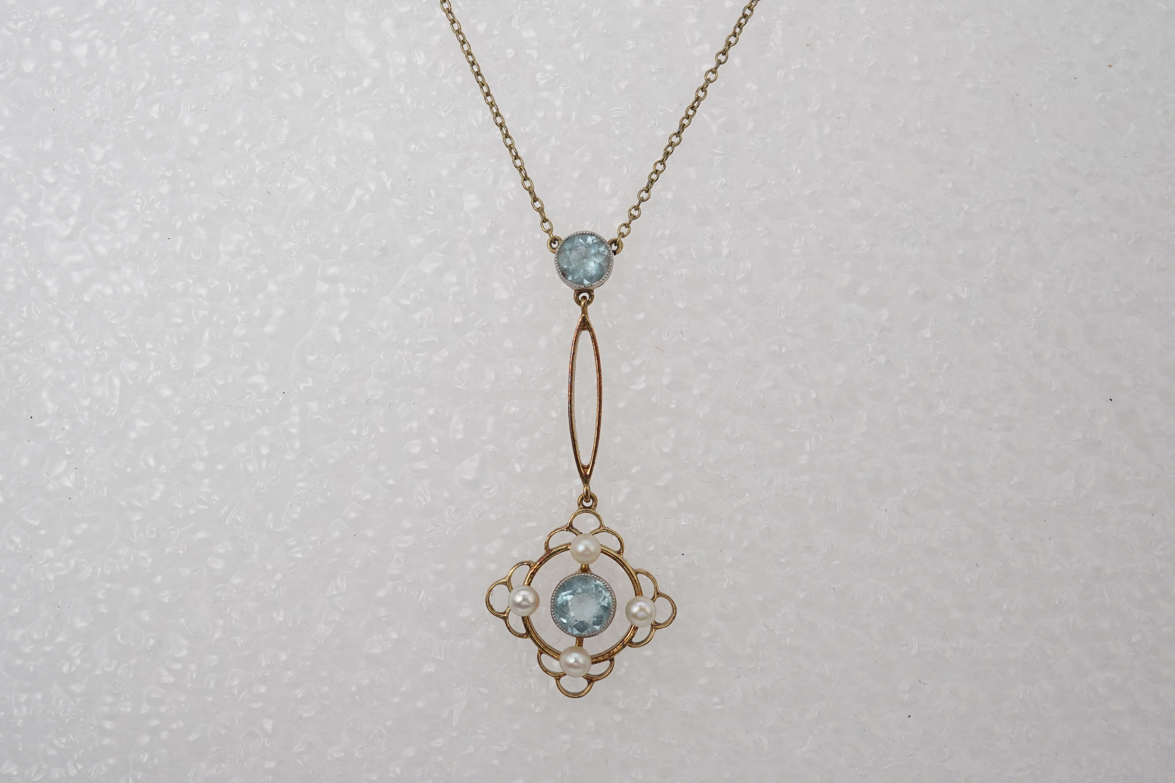 An Edwardian circular-cut aquamarine and seed pearl pendant, early 20th century, of foliate design, mounted in gold, pendant length 4cm, chain length 40cm, clasp stamped 15, gross weight approximately 3 grams, pearls unt